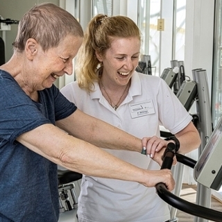 Patientin trainiert auf dem Ergometer und bekommt Anweisungen von der Therapeutin. Beide freuen sich über die Erfolge. Patientin trainiert auf dem Ergometer und bekommt Anweisungen von der Therapeutin. Beide freuen sich über die Erfolge.